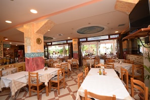 L’intérieur d’un restaurant, avec de nombreuses tables et chaises, un sol carrelé et un plafond doté d’un éclairage encastré.