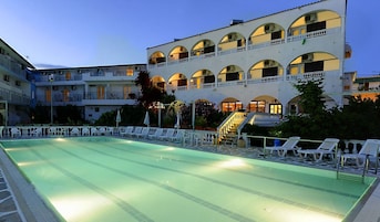 Una piscina con sillones de descanso y un edificio de varios pisos con balcones al fondo.