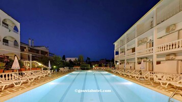 Una piscina con sillas de descanso y sombrillas, rodeada de edificios con balcones.