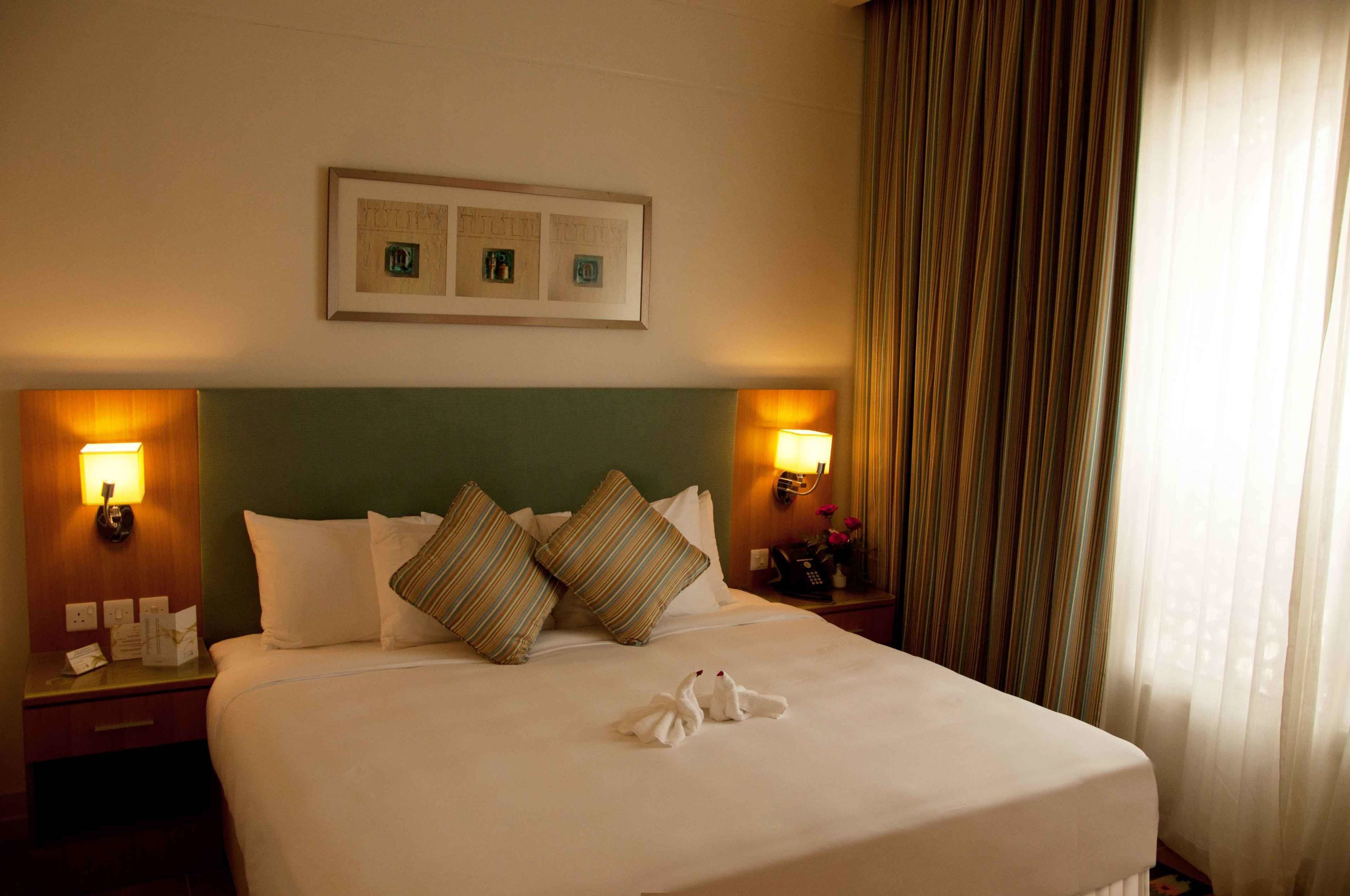 A hotel room with a neatly made bed, two bedside lamps, a framed picture on the wall, and a curtain on the window.