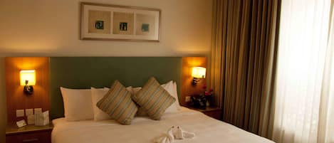 Habitación de hotel con una cama bien hecha, dos lámparas de noche, un cuadro en la pared y una cortina en la ventana.