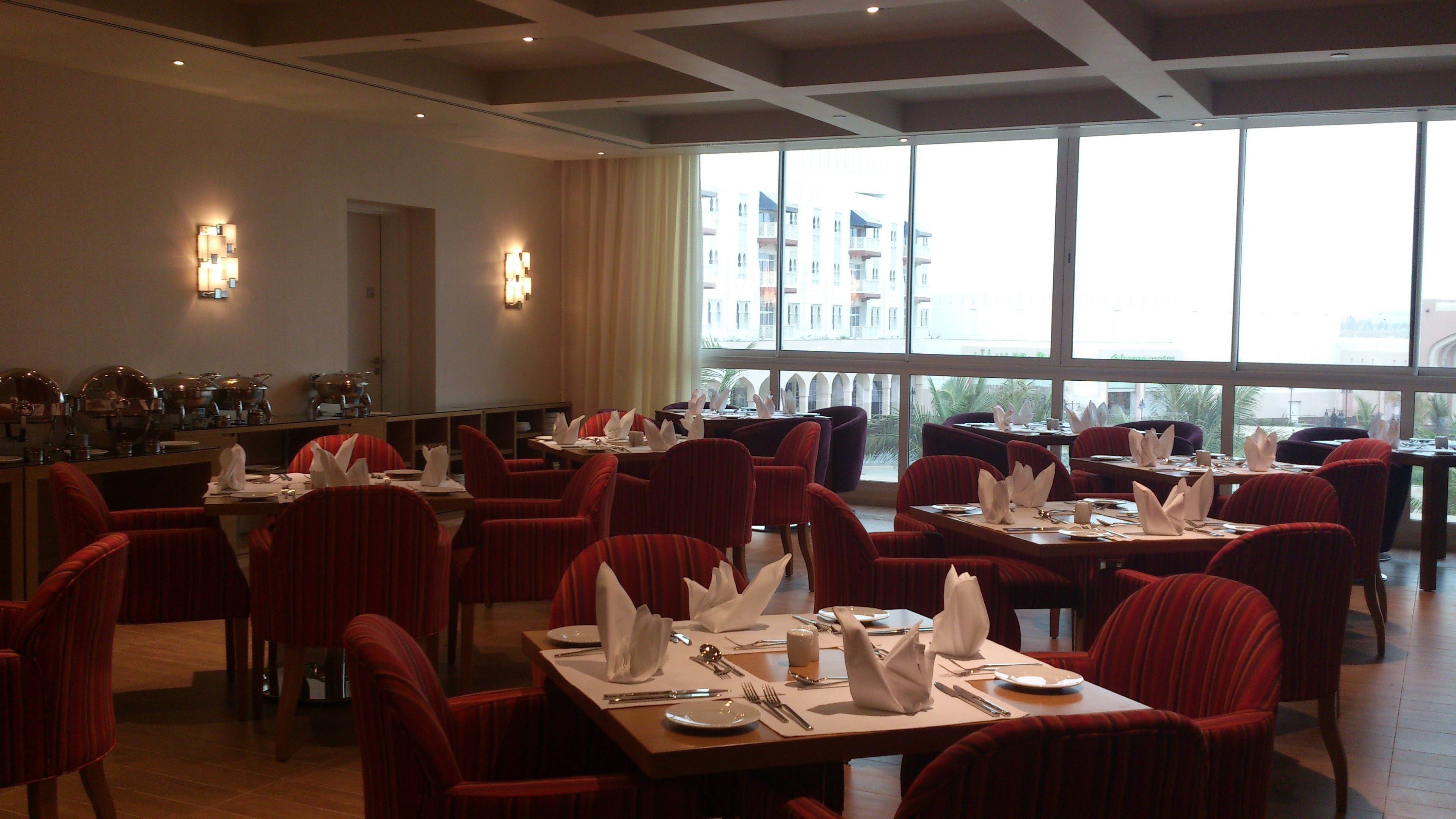 Ein Restaurant mit mehreren Tischen, Stühlen, großen Fenstern und Blick auf umliegende Gebäude.