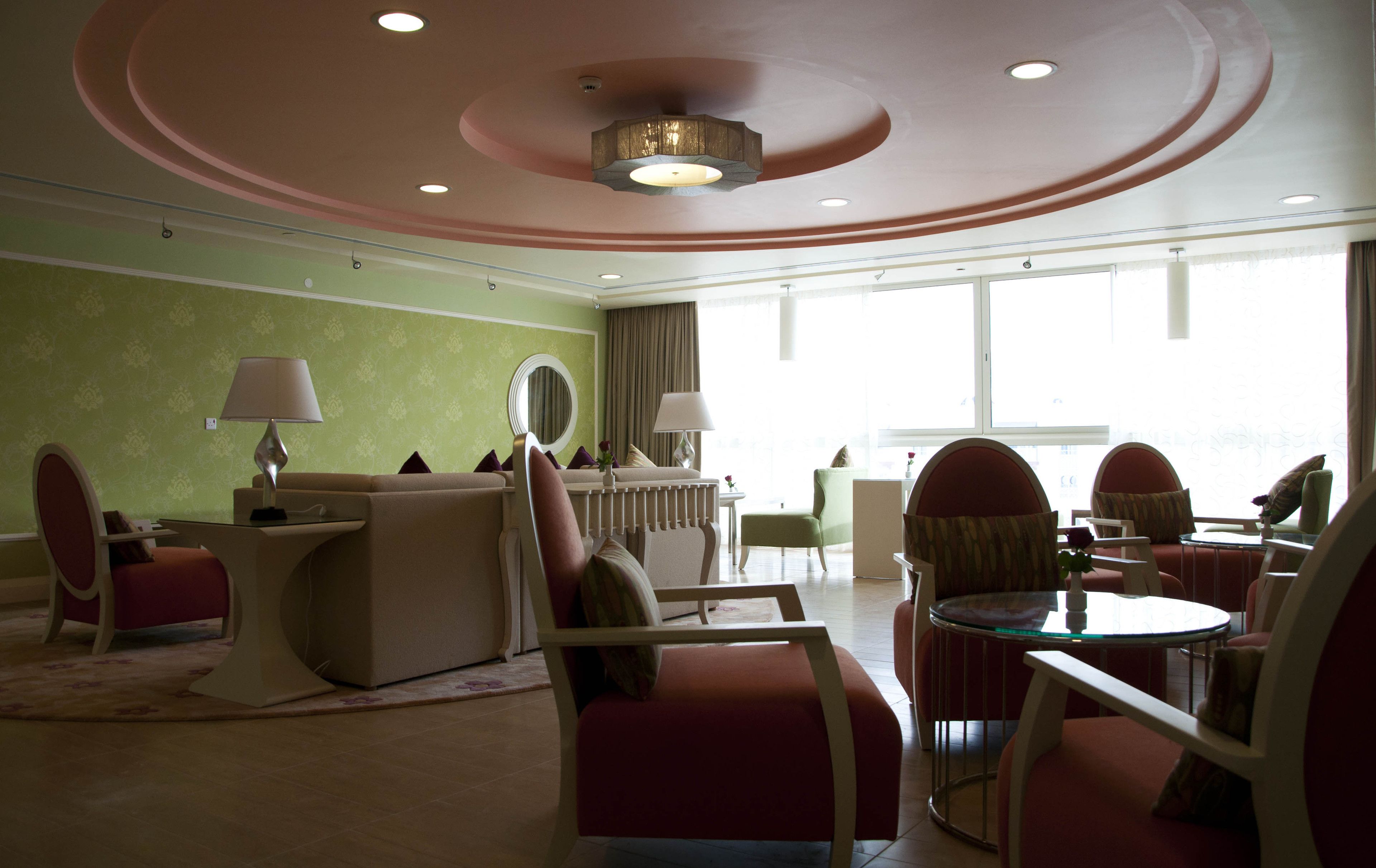 Un vestíbulo de hotel con una pared verde, un mostrador de recepción y zonas de estar con sillones y una mesa redonda.