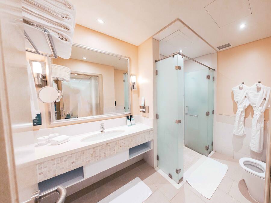 A modern bathroom with a large mirror, dual sinks, a glass shower enclosure, and a toilet.