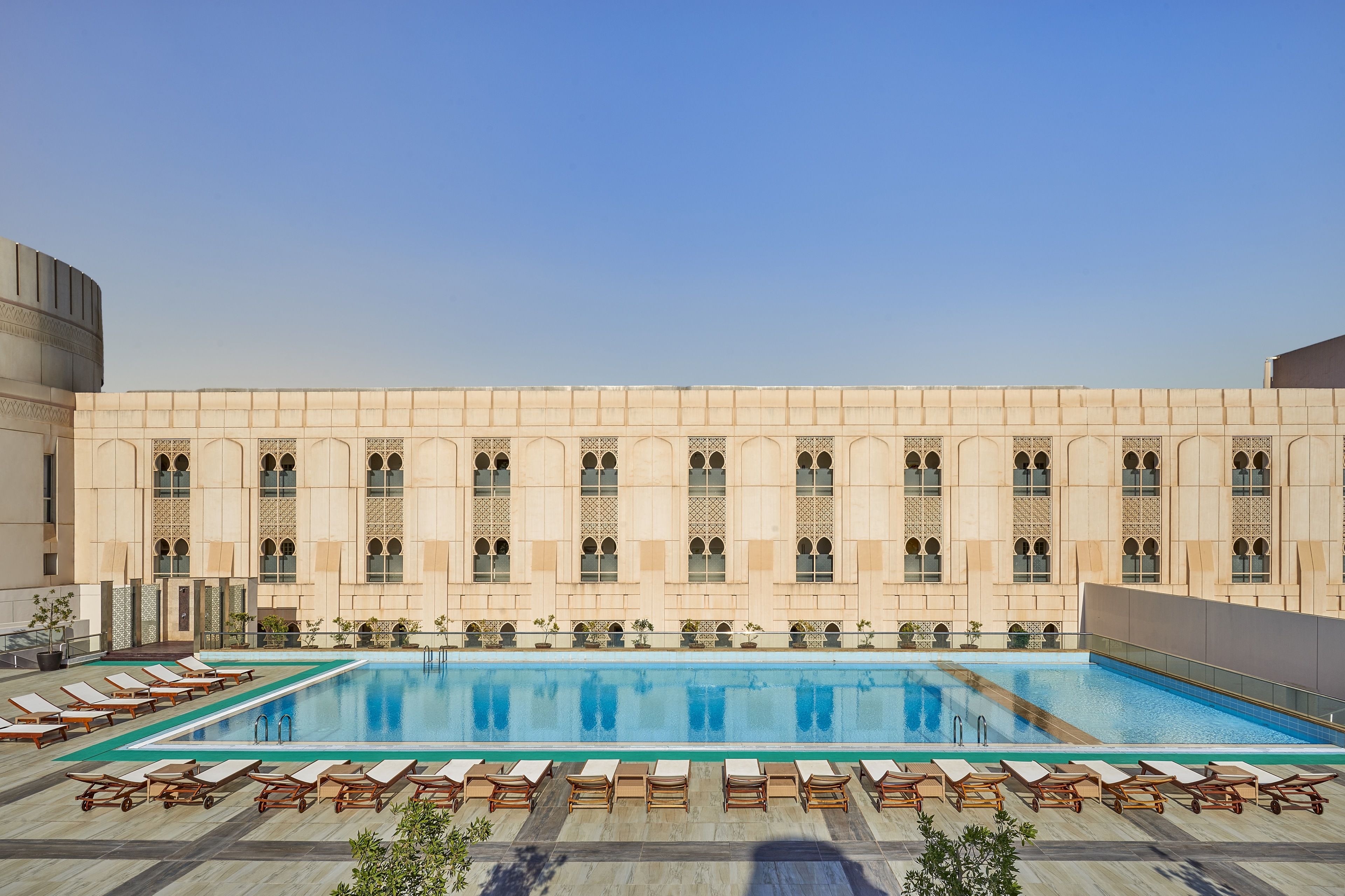 Una piscina en la azotea con tumbonas y un edificio con ventanales arqueados al fondo.