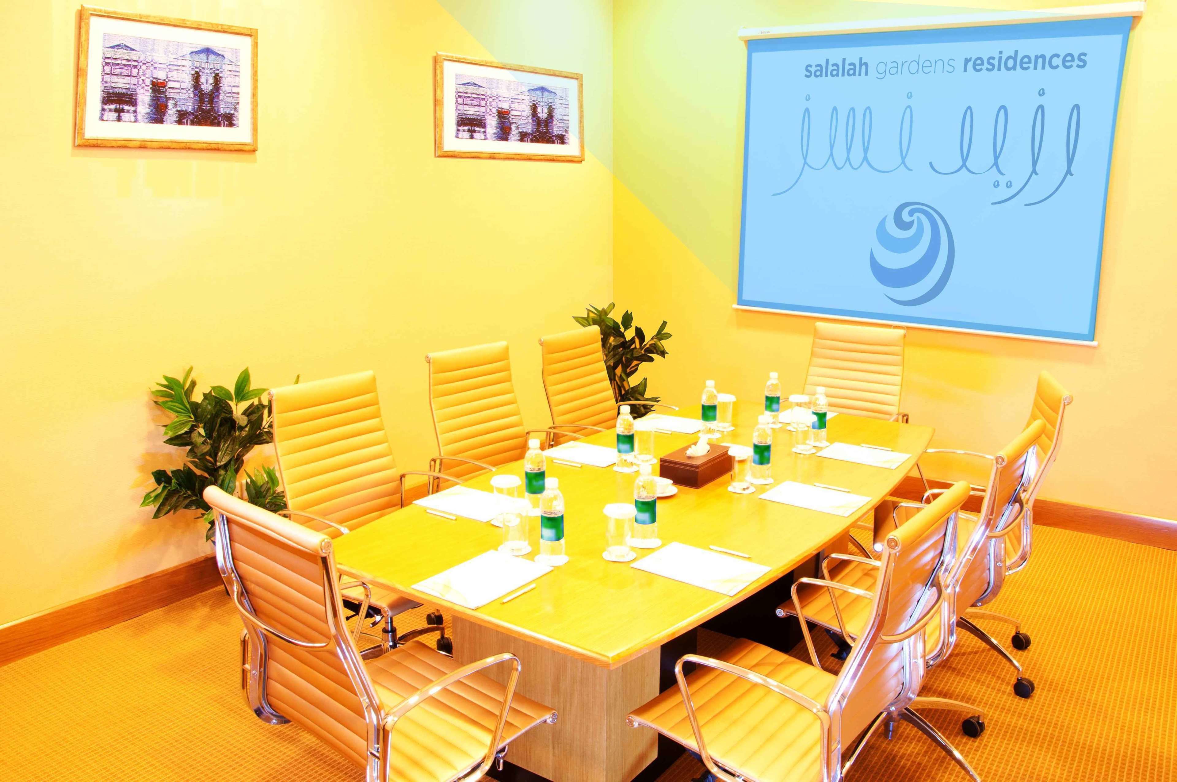A conference room with a yellow table, white chairs, and a projector screen displaying 'salah gardens residences'.