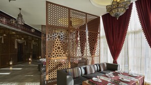 A spacious lobby with a modern sofa, a dining table set for four, and a decorative partition with intricate patterns. - Salalah Gardens Hotel Managed by Safir Hotels & Resorts  (Salalah)
