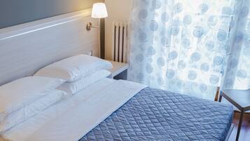 A neatly made bed with white and gray bedding, a bedside lamp, and a radiator.
