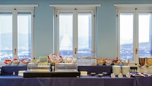 Montaje de bufé con diferentes opciones de comida y una exhibición de tés, con grandes ventanales que dan a una vista panorámica de la ciudad.