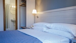 Una cama bien hecha con sábanas blancas, una lámpara de noche y una mesita de noche con un teléfono.