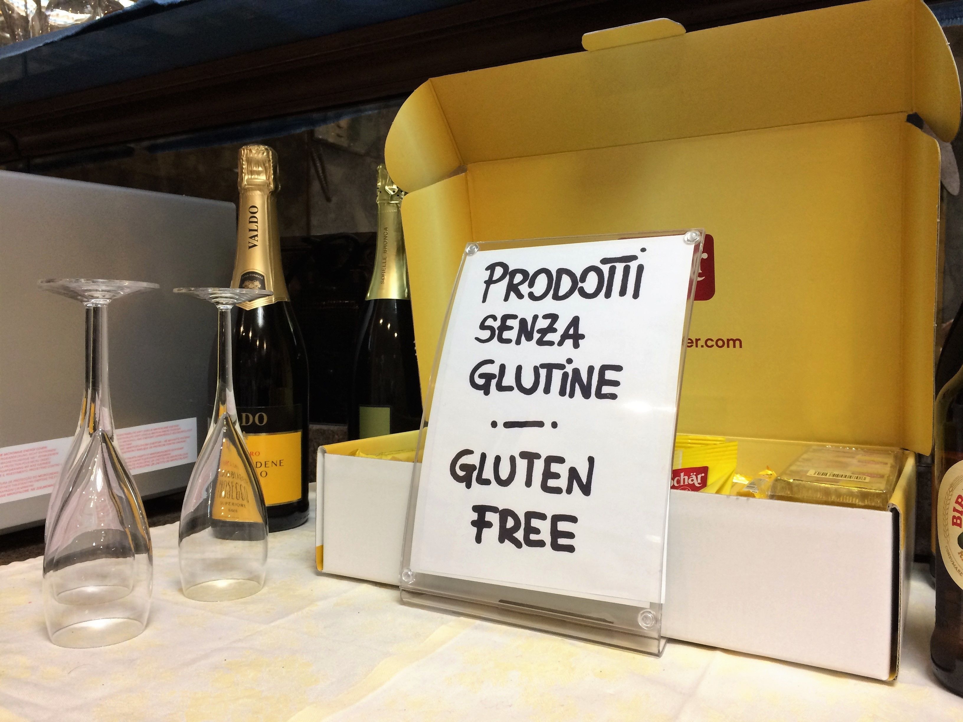 Una exhibición con botellas de vino y un cartel que dice 'PRODOTTI SENZA GLUTINE - GLUTEN FREE'.