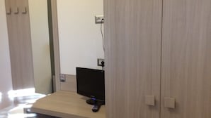 Una habitación compacta con un escritorio de madera, un monitor de computadora, un refrigerador pequeño y un armario.