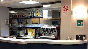 Zona de bar con mostrador, taburetes y una variedad de botellas y vasos.