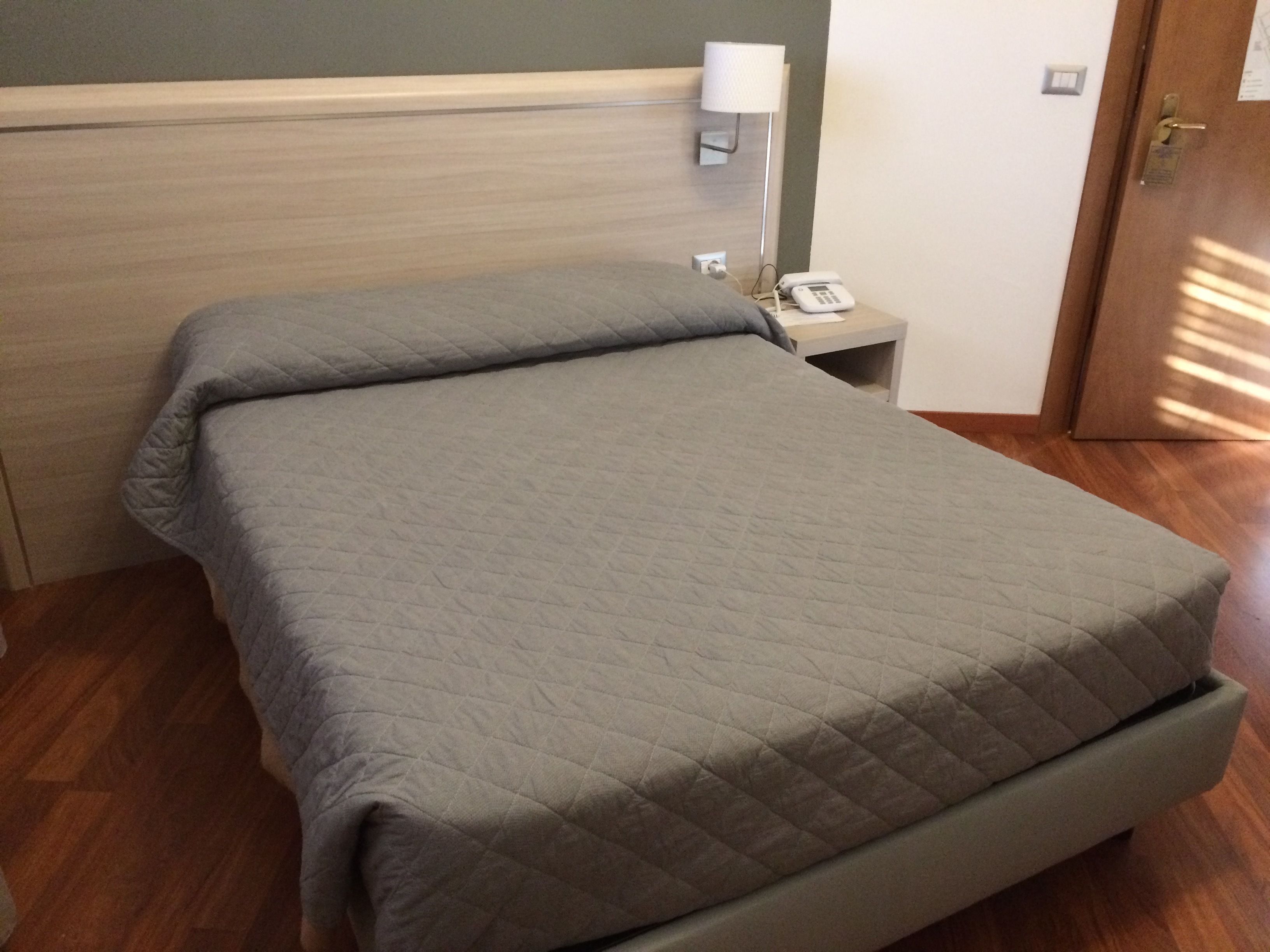 Un letto ben rifatto con copriletto trapuntato, un comodino con lampada e telefono.