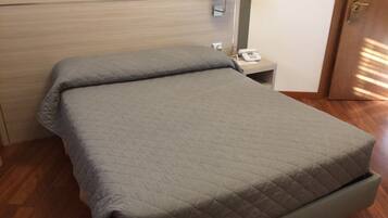 Un letto ben rifatto con copriletto trapuntato, un comodino con lampada e telefono.