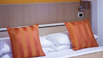 Habitación de hotel con cama, dos almohadas a rayas, cabecera blanca, lámpara de pared y termostato.