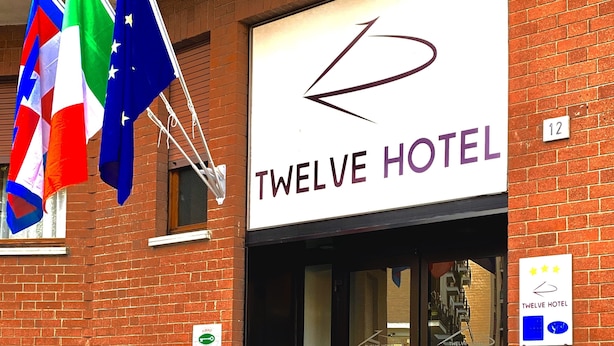 Exterior del Hotel Twelve, con un letrero visible, fachada de ladrillo y dos grandes macetas.