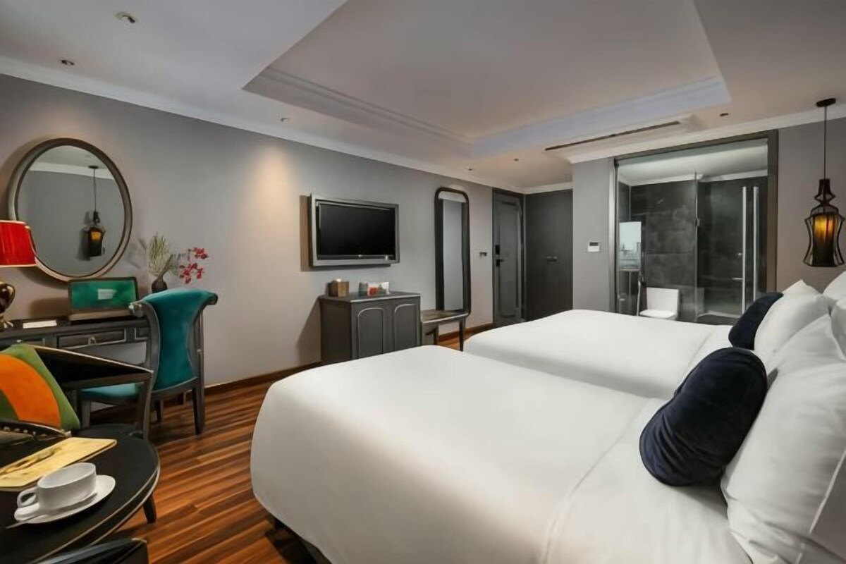 A hotel room with a bed, a desk with a chair, a TV, a mirror, and a sliding door to a balcony.