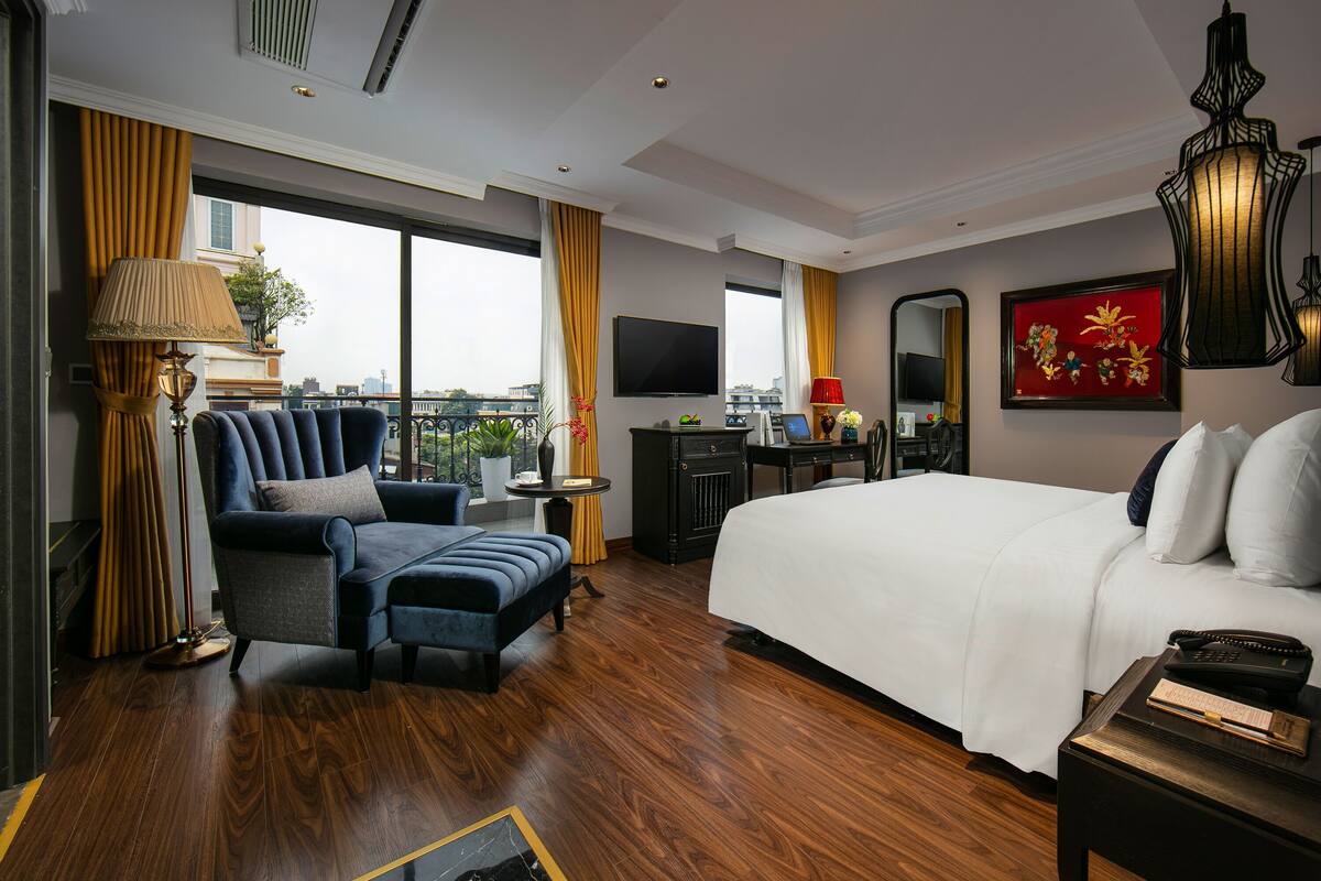 A hotel room with a large bed, a sofa, a desk, and a TV.