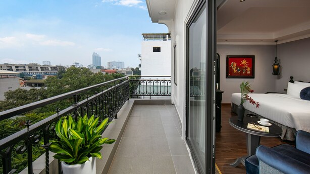 Un balcón con vistas a la ciudad, una cama, una mesa con un jarrón y una silla.