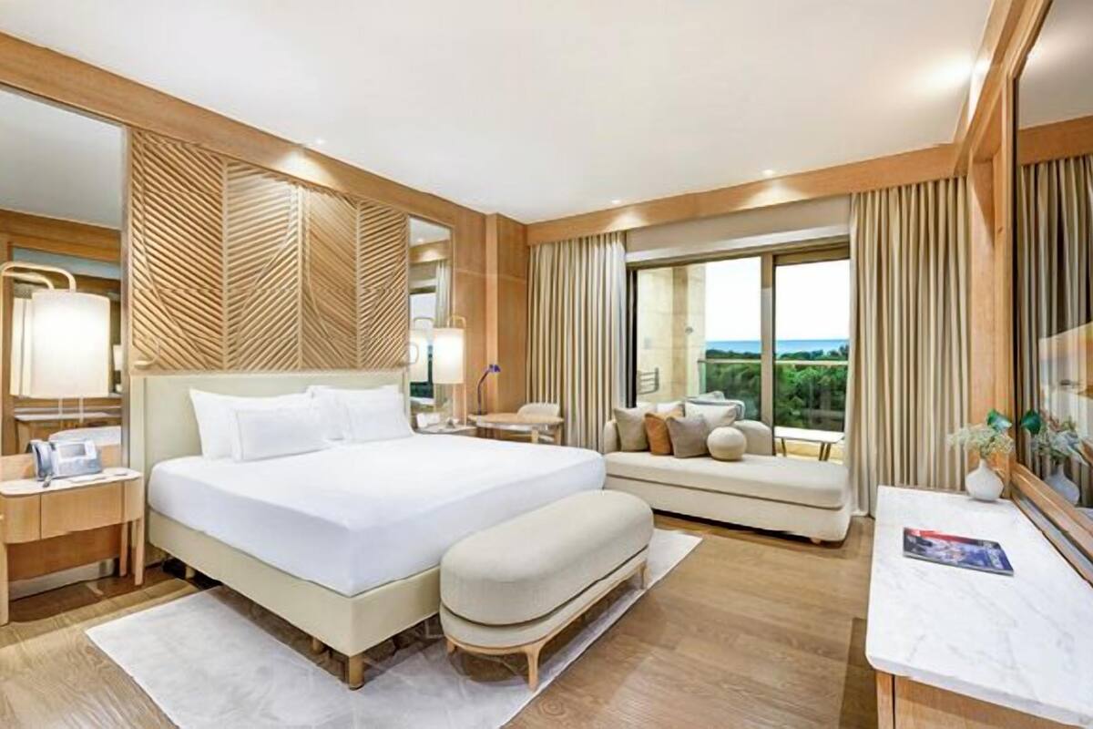 A hotel room with a large bed, a sofa, a desk, and a large window with a view.