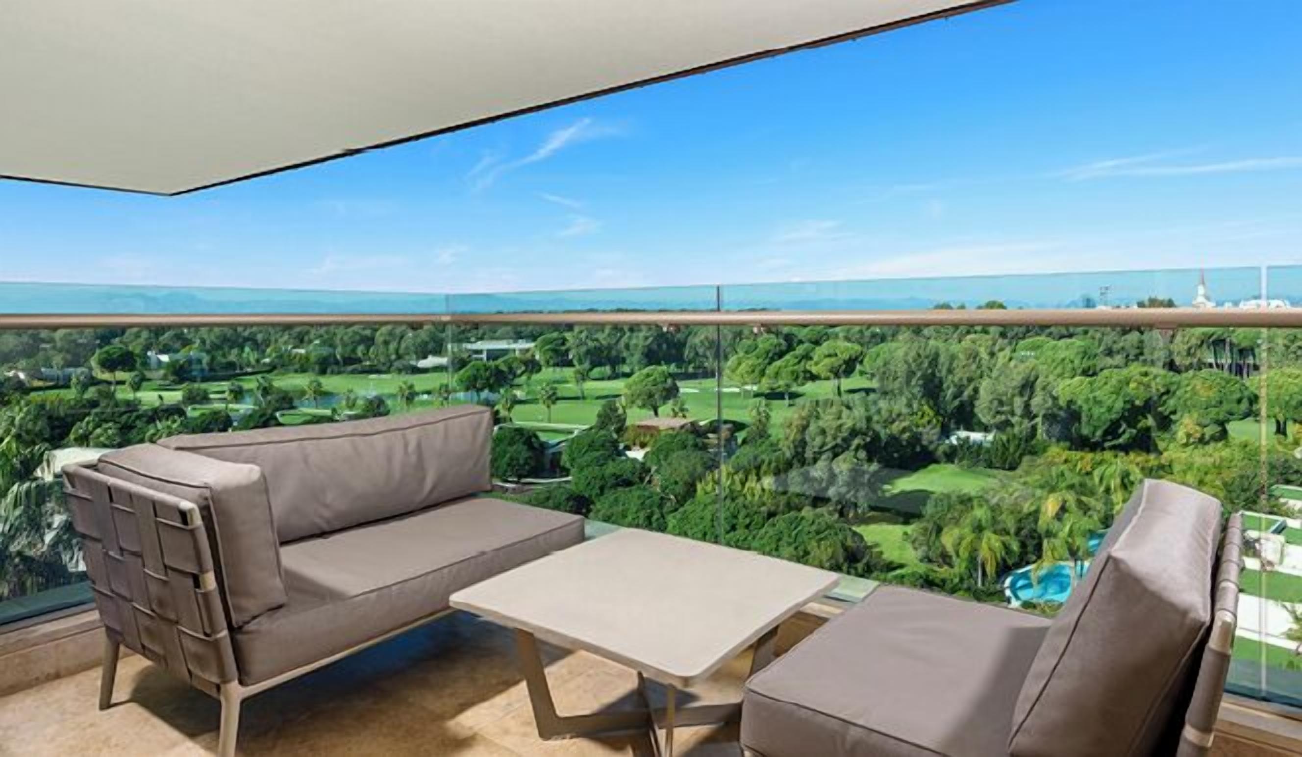 Een balkon met een bank en tafel, met uitzicht op een groen landschap en een waterpartij.