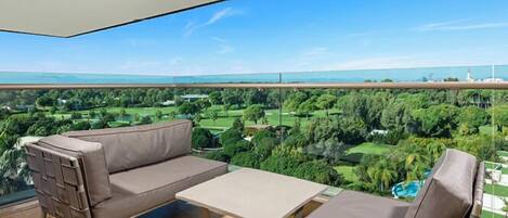 Een balkon met een bank en tafel, met uitzicht op een groen landschap en een waterpartij.