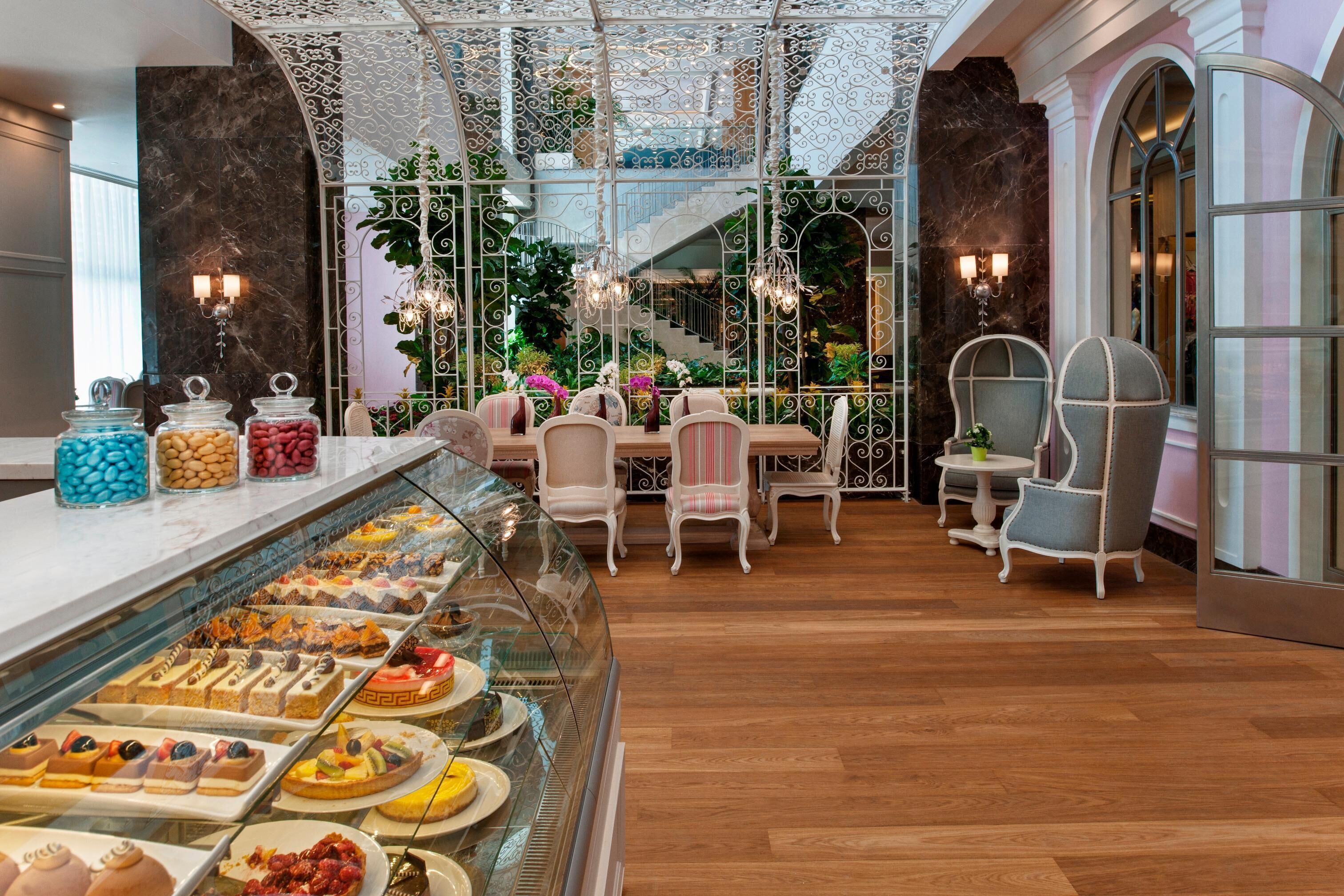 A luxurious hotel lobby with a dessert display, elegant seating, and a staircase leading to a balcony.