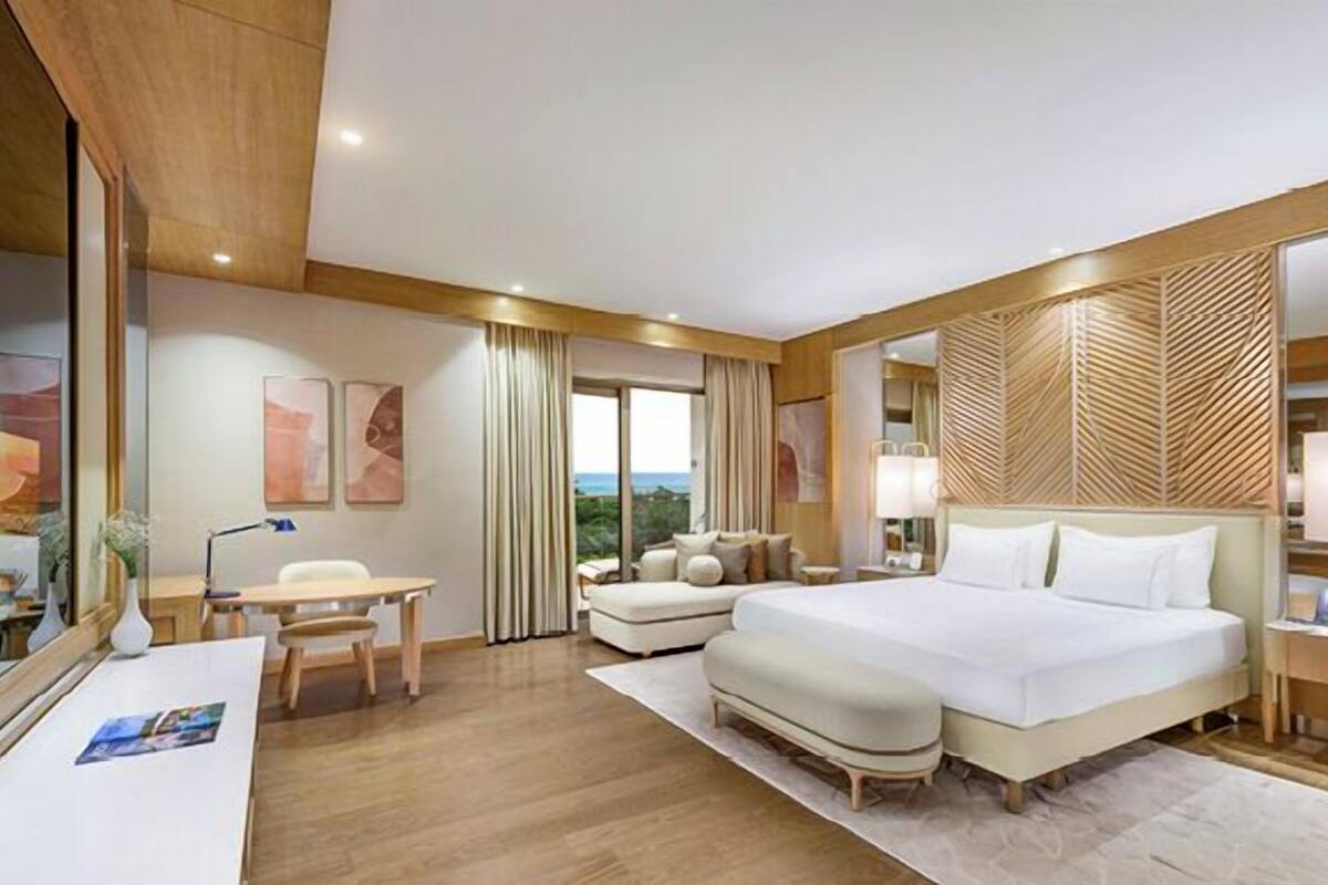 A hotel room with a large bed, a desk, a chair, a sofa, and a view of the outdoors.
