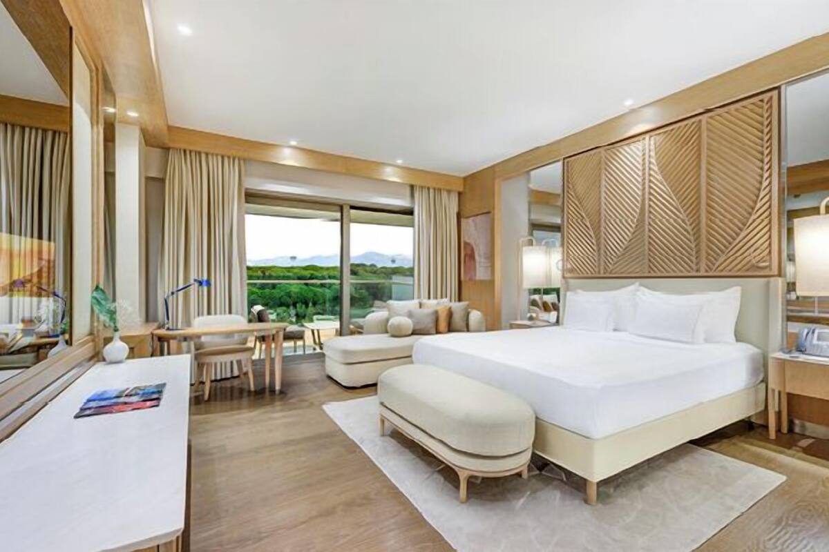 A hotel room with a large bed, a desk, a chair, and a view of the outdoors.
