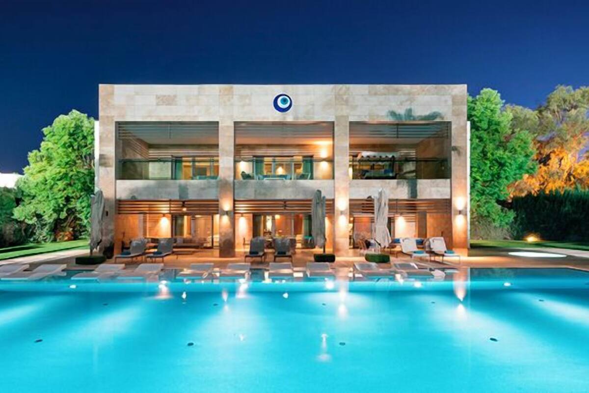 A modern hotel with a large pool, outdoor seating, and a well-lit facade.