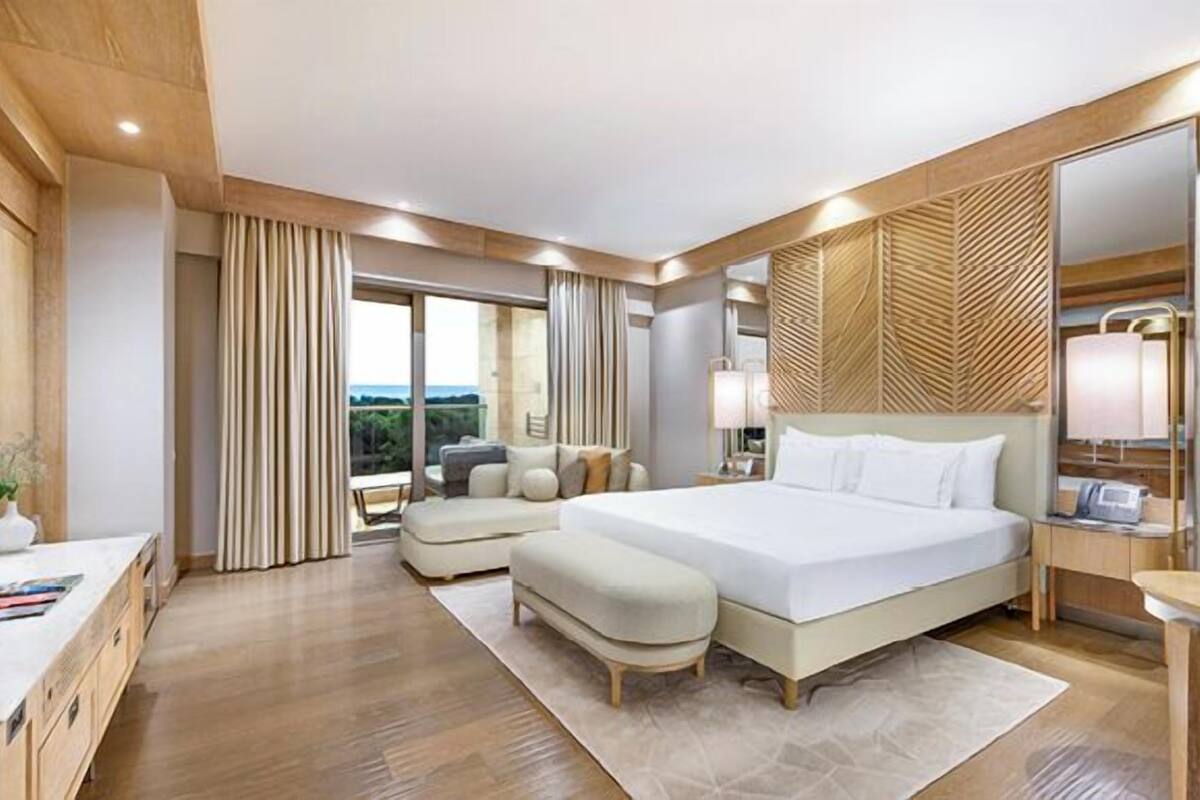 A modern hotel room with a large bed, a desk, a sofa, and a view of the outdoors.