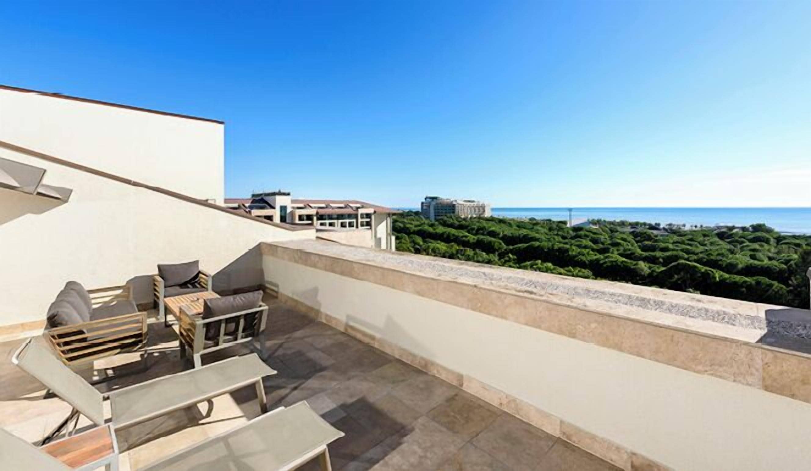 Una terraza en la azotea con mobiliario exterior, vista al mar y edificios al fondo.
