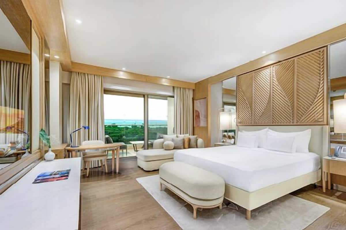 A hotel room with a large bed, a desk, a chair, a sofa, and a view of the outdoors.