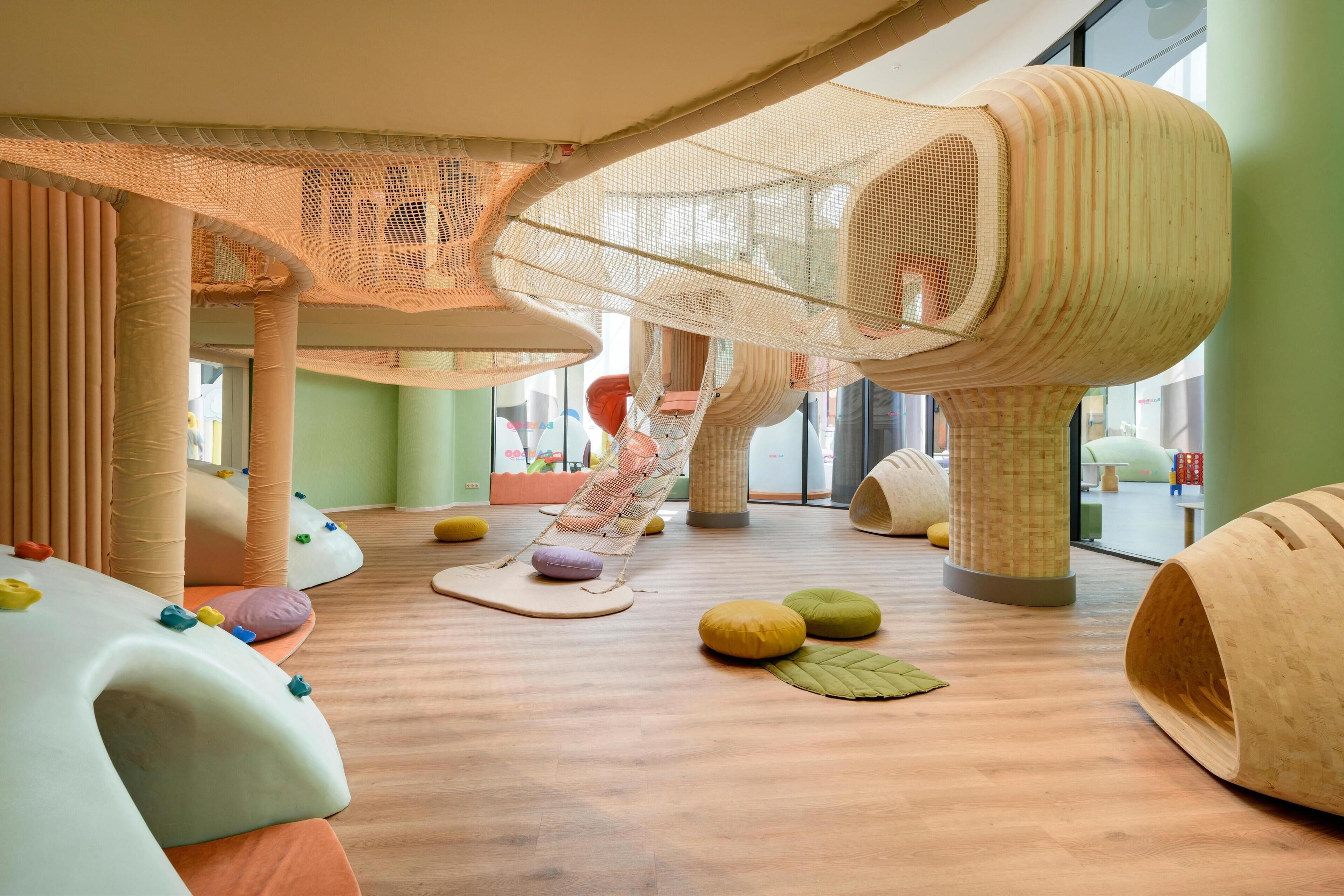 A play area with soft play structures, a hanging net, and colorful cushions.