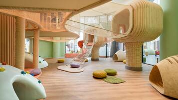 A play area with soft play structures, a hanging net, and colorful cushions.