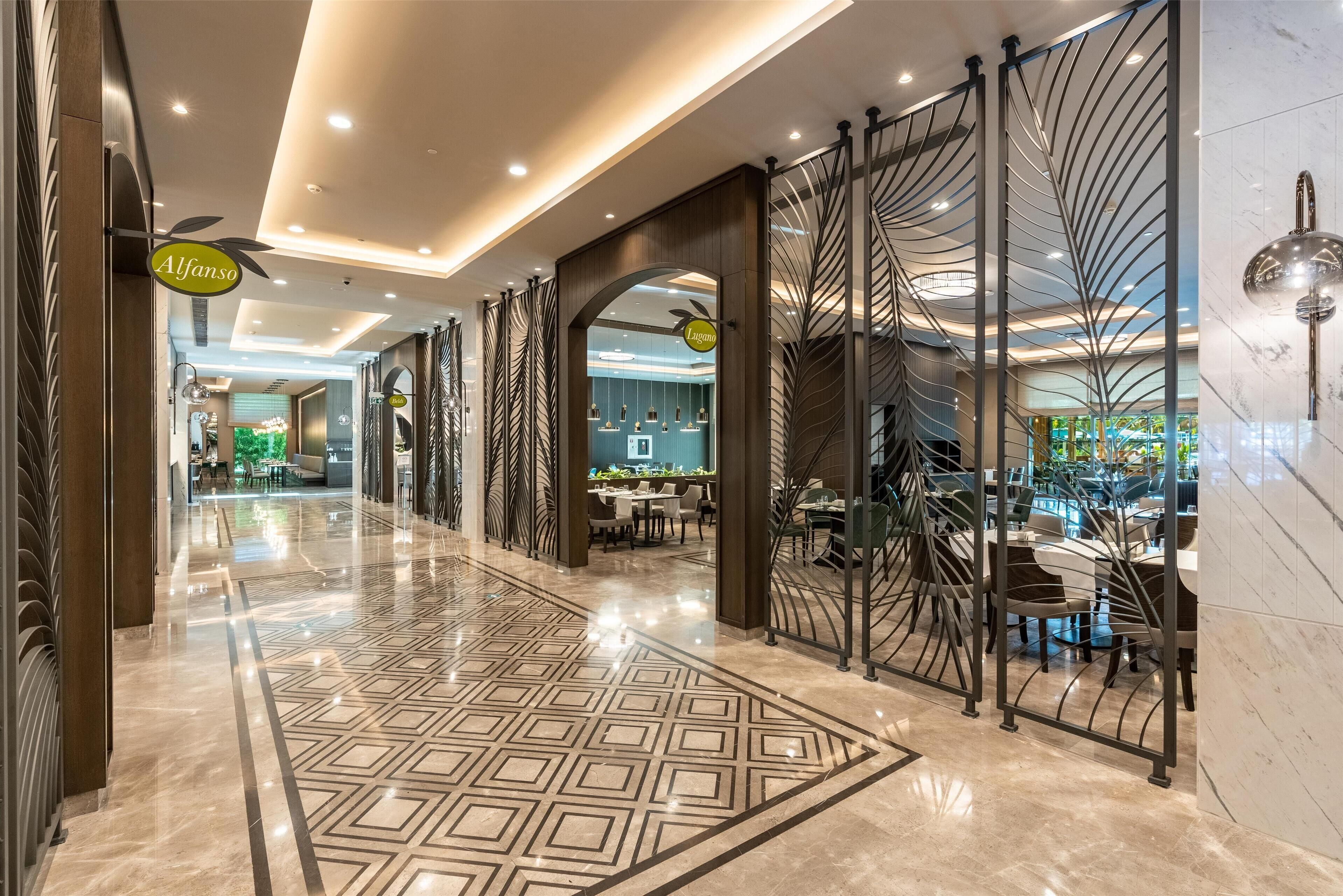 A hotel lobby with a polished marble floor, a reception area, and a dining space.