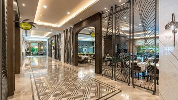 A hotel lobby with a polished marble floor, a reception area, and a dining space.