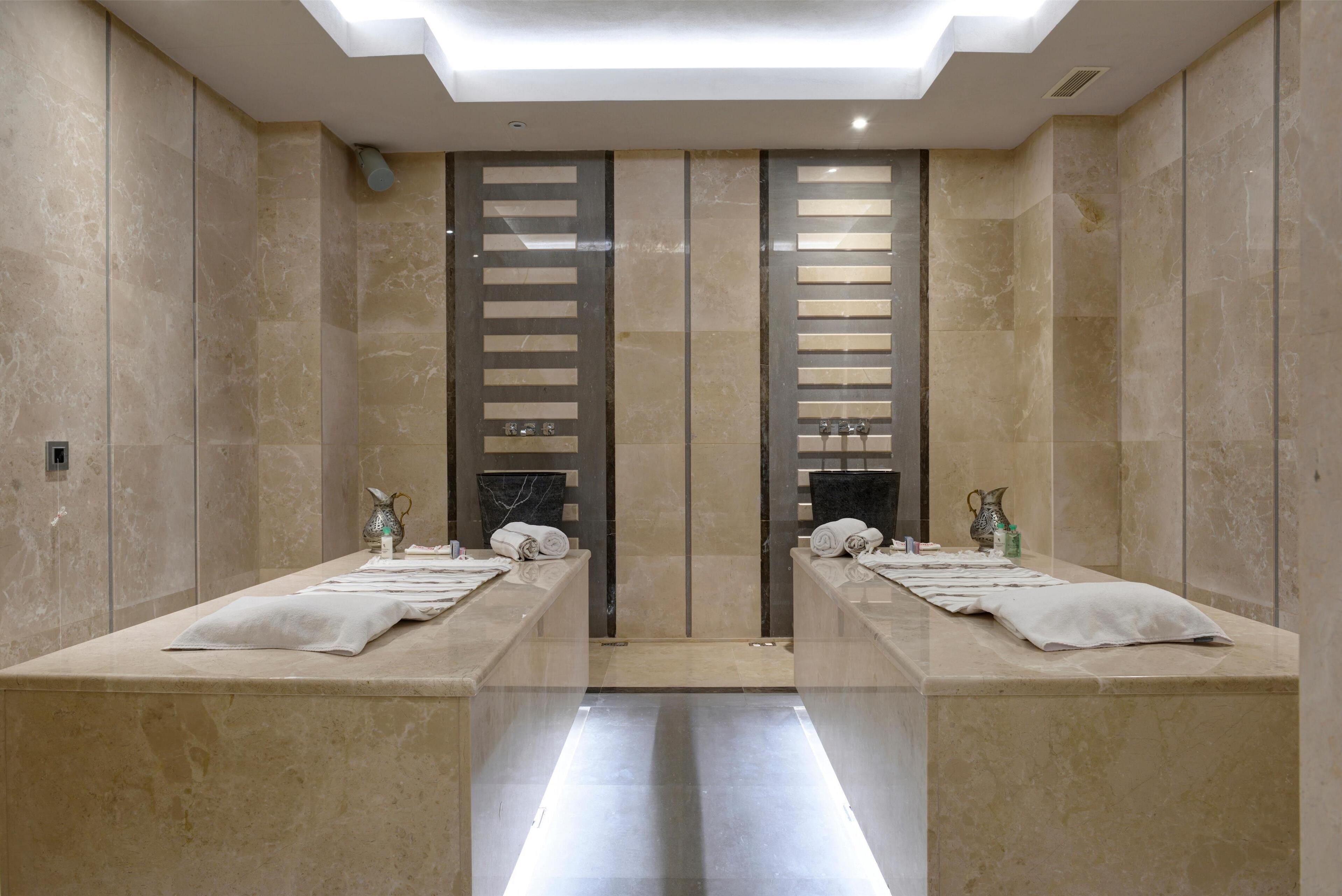 A modern bathroom with two sinks, marble walls, and a skylight.