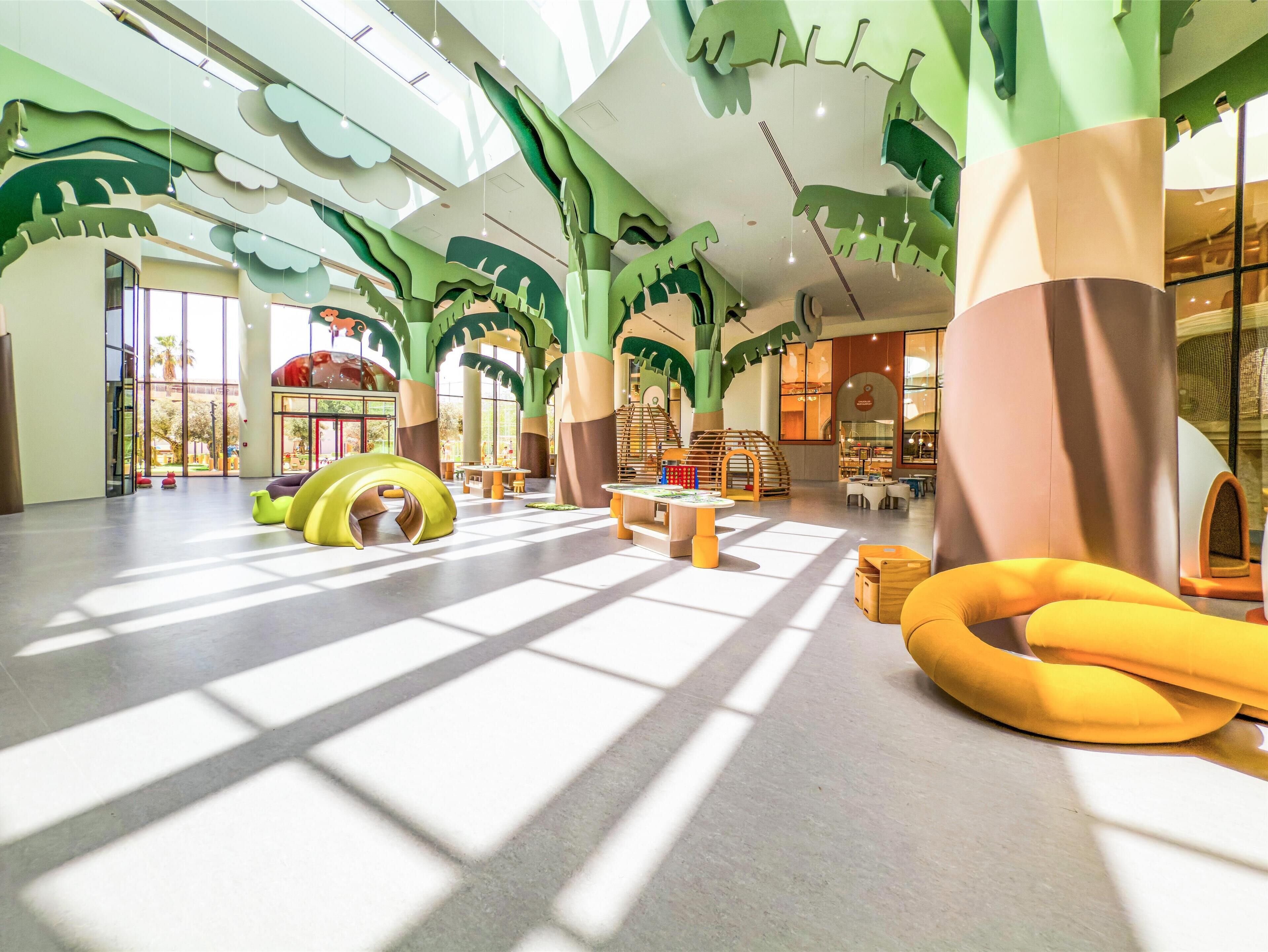 Un espacio interior amplio con techos altos, ventanas grandes que dejan entrar luz natural y decoración juguetona con motivos de árboles.