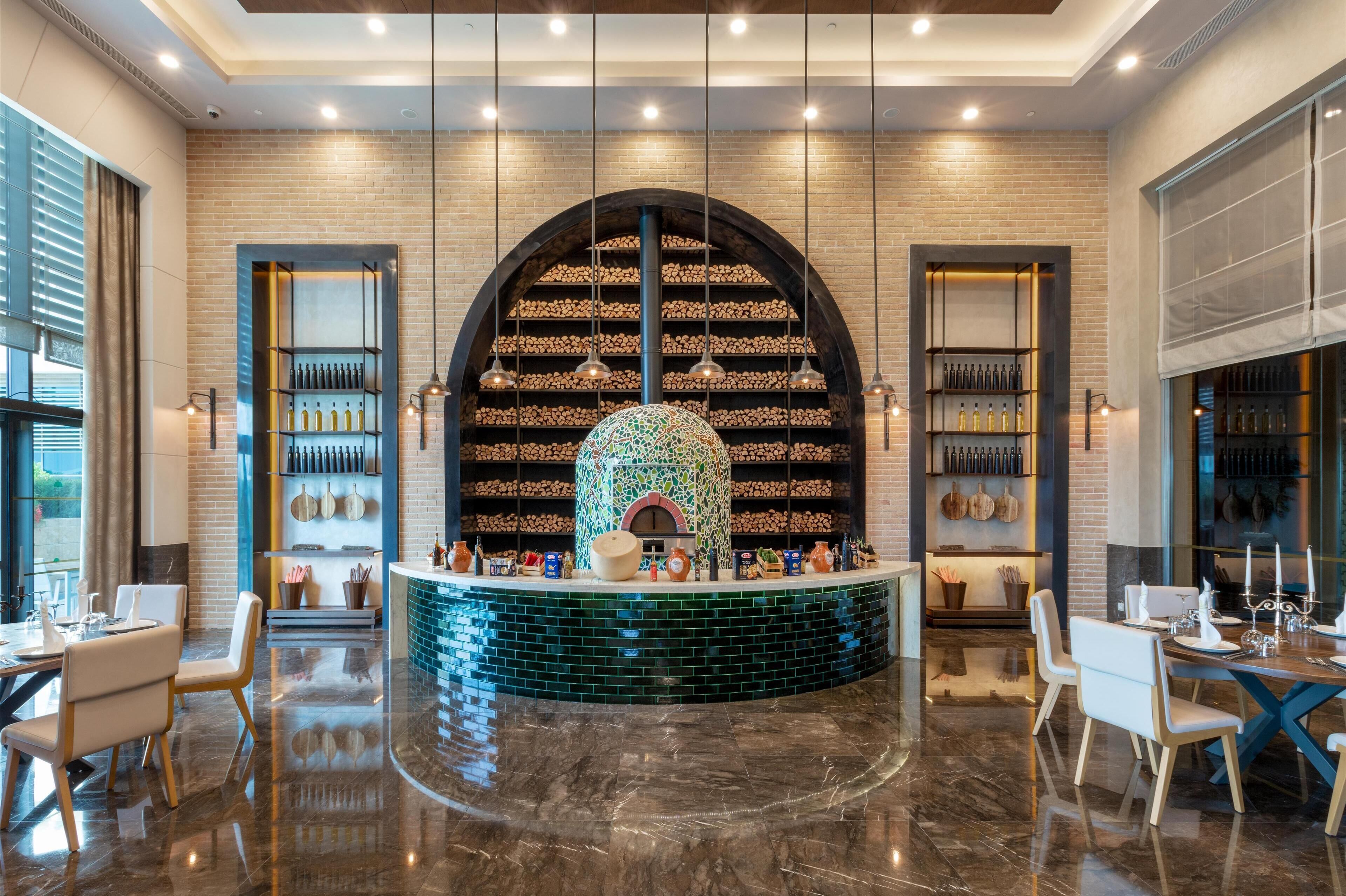 A restaurant with a central seating area, a brick wall with shelves of bottles, and a decorative tile wall.