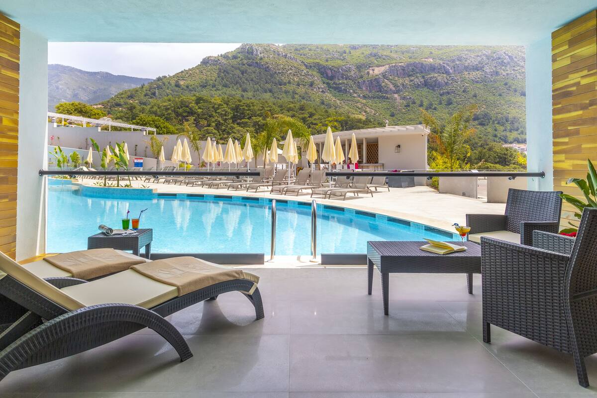 A poolside area with lounge chairs and umbrellas, a clear view of a mountainous landscape, and a pool.