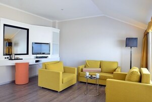 Una sala moderna con dos sofás amarillos, una mesita redonda, un televisor y una lámpara de pie.