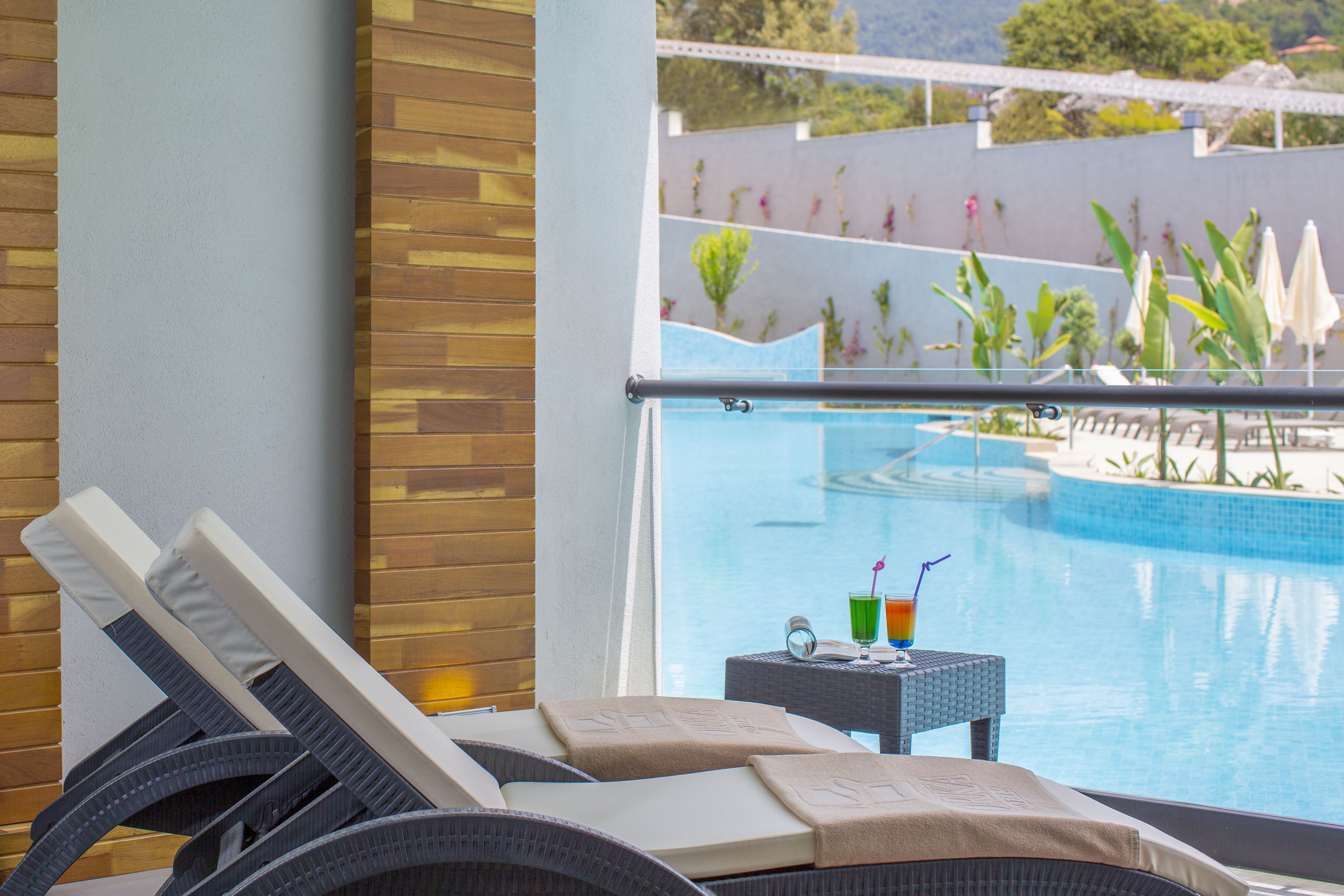 A poolside area with lounge chairs, a small table with drinks, and a view of the pool and surrounding greenery.