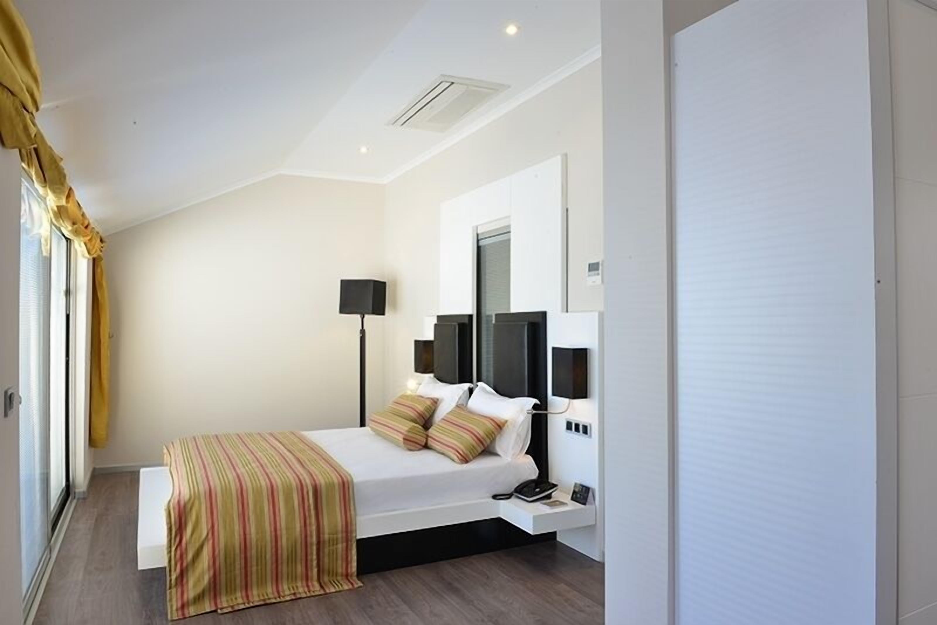 Een moderne slaapkamer met een bed, nachtlampjes, een spiegel en een raam met gordijnen.