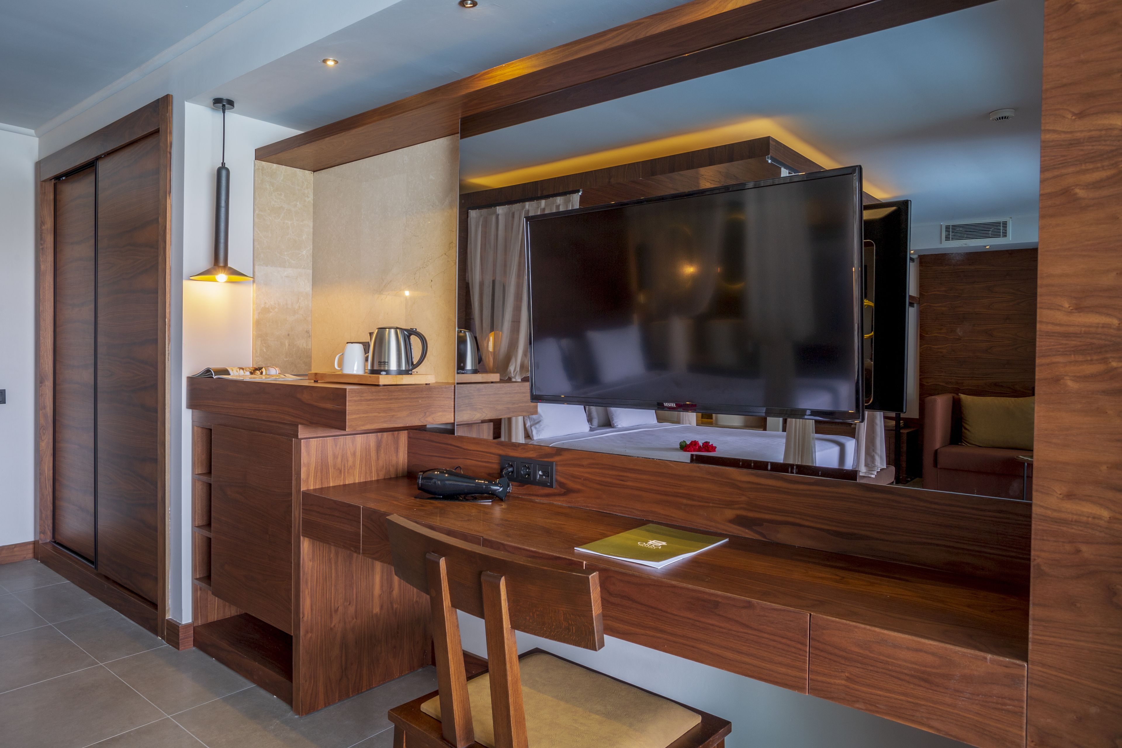 A modern hotel room with a wooden desk, a flat-screen TV, a coffee maker, and a laptop.
