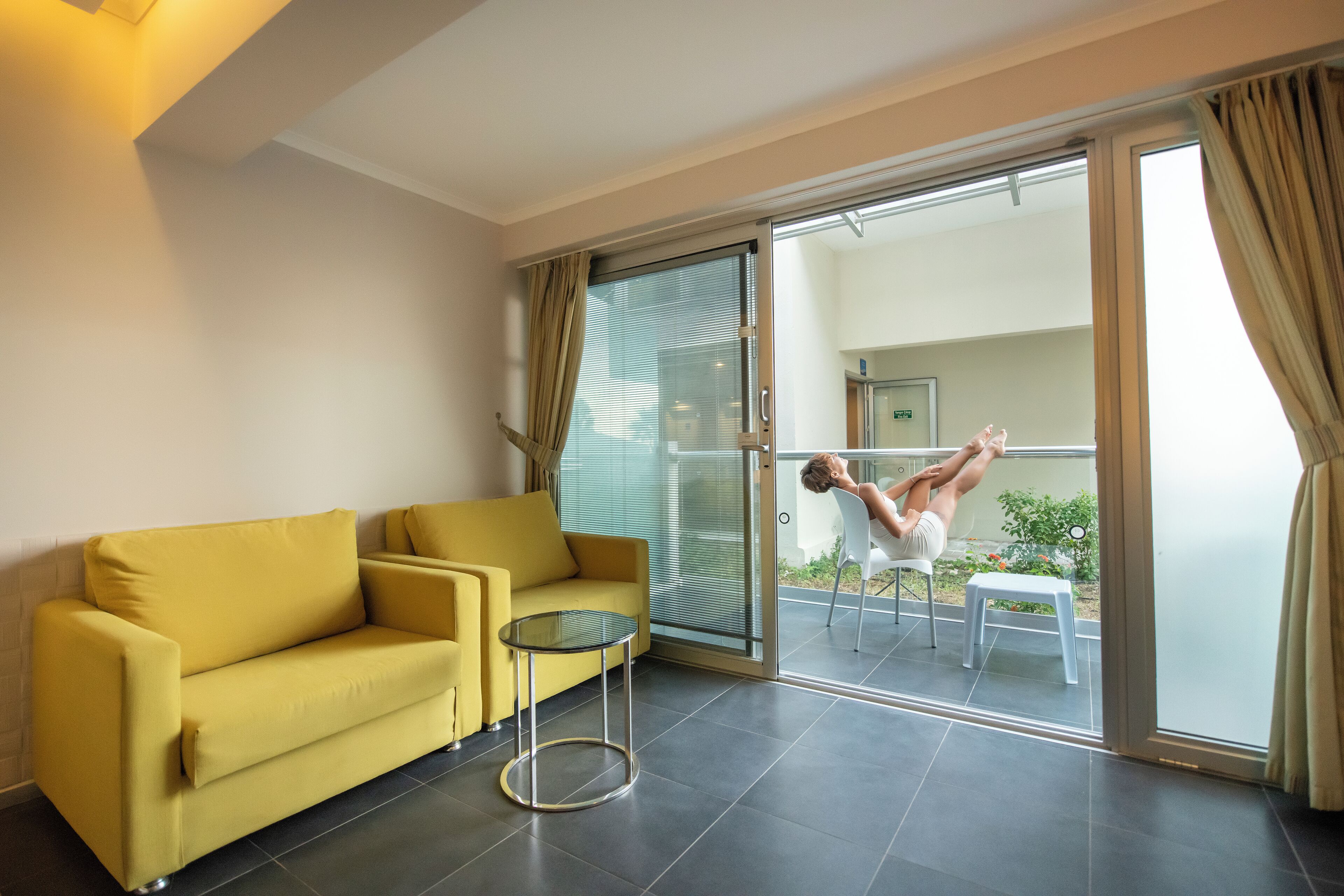 A modern living room with a yellow sofa, a small round table, and a glass door leading to a balcony.