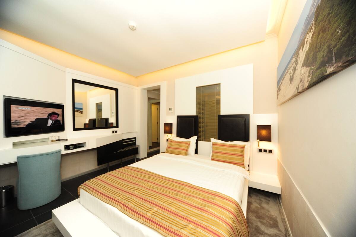 A modern hotel room with a large bed, a flat-screen TV, a desk, and a mirror.