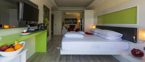 A modern hotel room with a bed, a green desk, a fruit bowl, and a television.