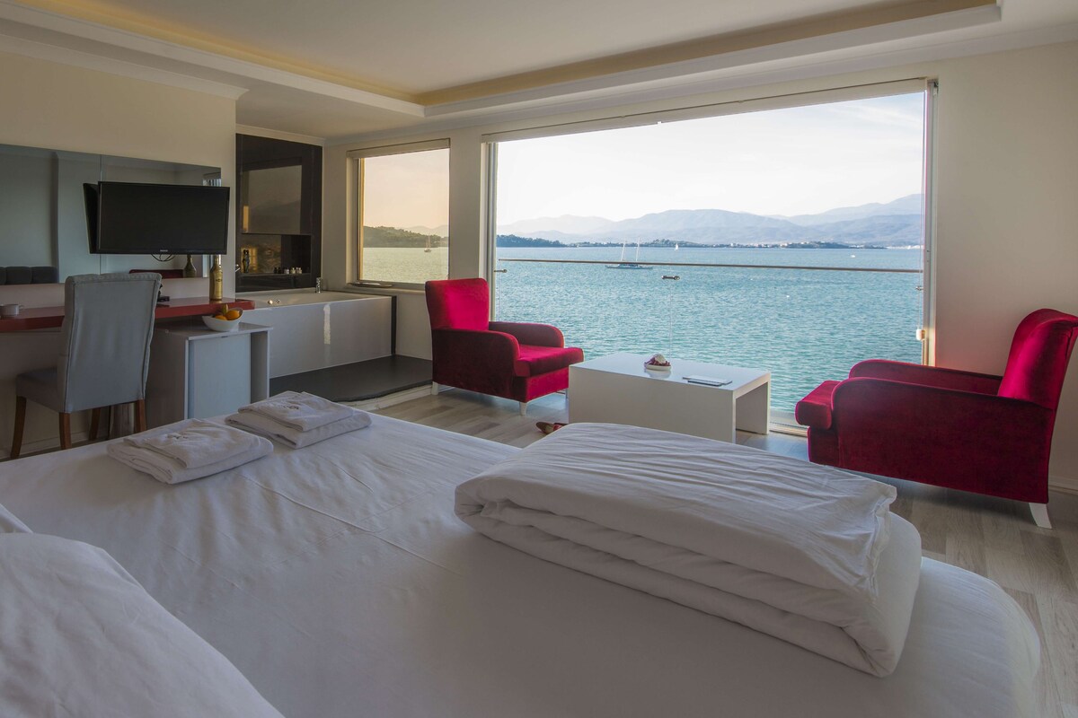 A hotel room with a bed, a desk, a chair, a TV, and a view of the water.